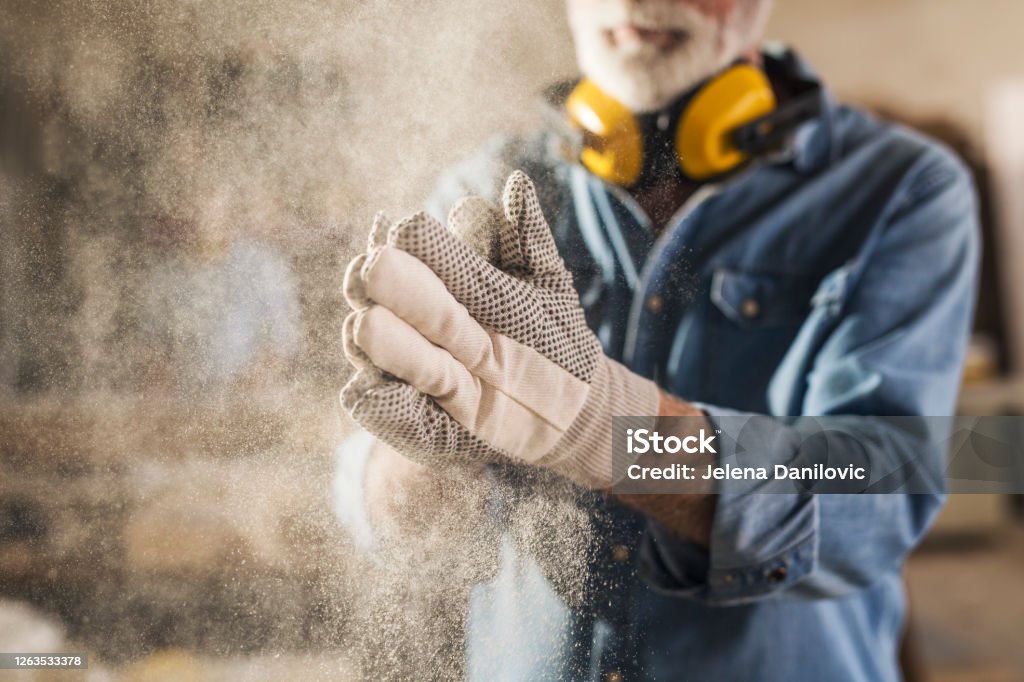 Carpenter cleaning work gloves Carpenter cleaning work gloves from sawdust after he finished processing the wood Dust Stock Photo