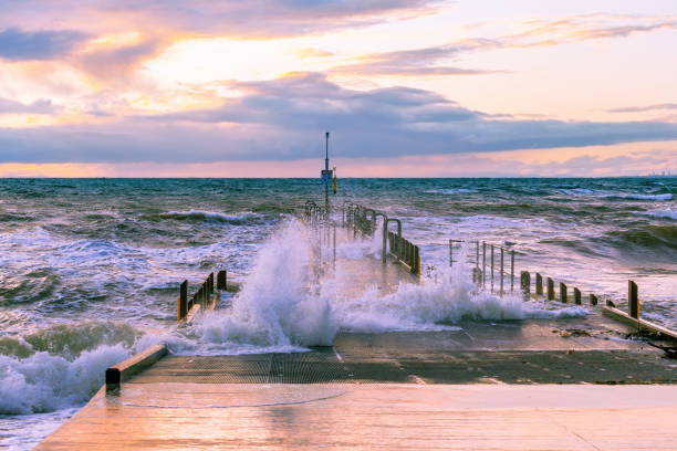 Large wave splashes protruding through boat jetty on ocean coastline at sunset Large wave splashes protruding through boat jetty on ocean coastline at sunset ebb and flow stock pictures, royalty-free photos & images