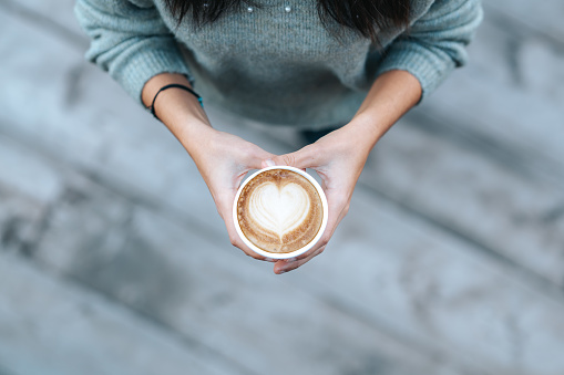 Young woman holding disposable cup with heart shaped coffee in a cafe. High quality photo
