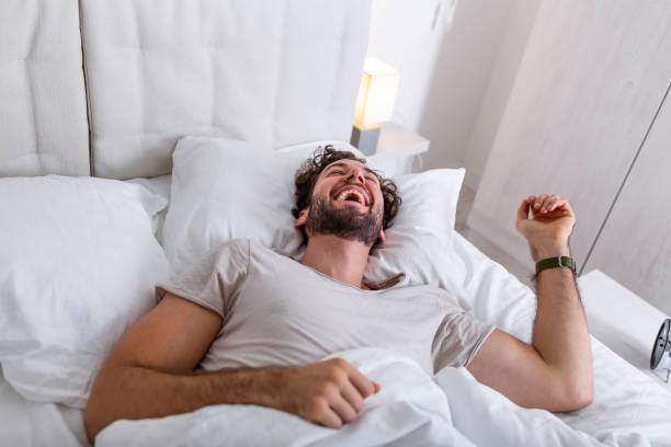 istock Young man sleeping waking up and stretching in his bed. people, bedtime and rest concept - man lying in bed at home, It's time to wake up 1263539068