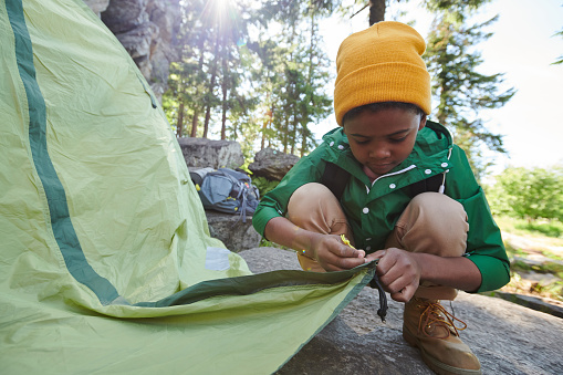 African little boy setting up the tent during camping  in the nature