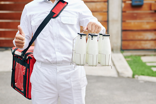 Cropped image of delivery man holding wire crate with glass milk bottles and showing thumbs-up