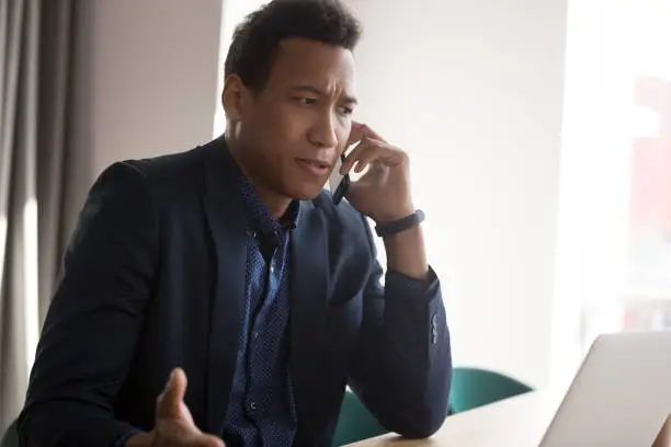 Photo of Angry black businessman disputing on phone at office