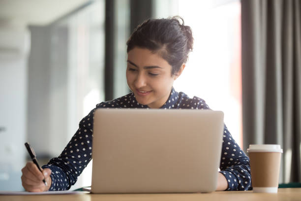 istock Smiling indian businesswoman making notes during video call at office. 1263550266