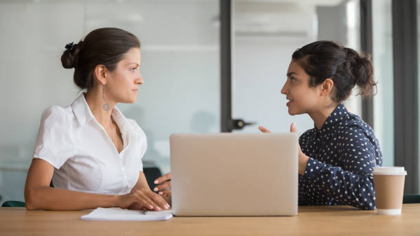 Diverse business woman team discussing work issues Enthusiastic young indian employee sharing new project ideas with serious female boss. Diverse business woman team discussing working moments at office. HR manager listening to interns experience bossy stock pictures, royalty-free photos & images