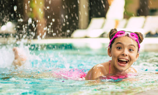 szczęśliwa piękna mała uśmiechnięta dziewczyna w goglach i stroju kąpielowym w basenie bawi się podczas wakacji lub lekcji pływania. - swimming child swimming pool indoors zdjęcia i obrazy z banku zdjęć