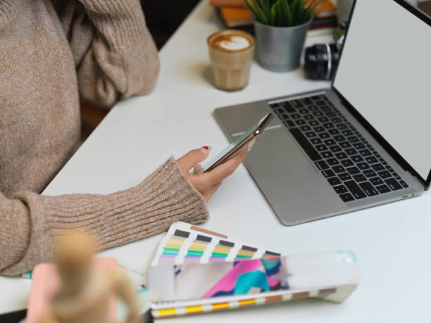 istock Female designer in sweater using smartphone on office desk 1263553054
