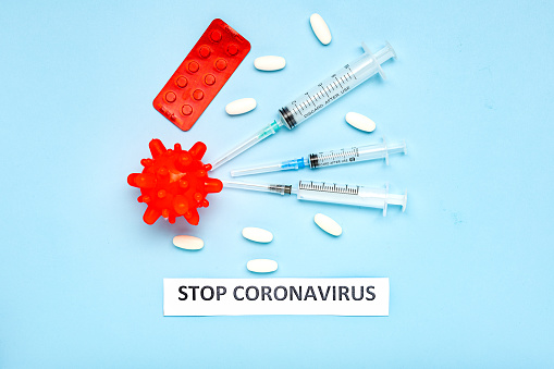 Medicines against Coronavirus model. Different pills, syringes, text STOP CORONAVIRUS. 2019 nCoV coronavirus on blue background with copy space. COVID-19, COVID-19 outbreak influenza