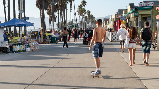 Venice Beach, Los Angeles, California, US - September 30, 2017: young man on a skateboard through the famous boardwalk lined with lots of restaurants, souvenir shops, a skate park and an outdoor gym.