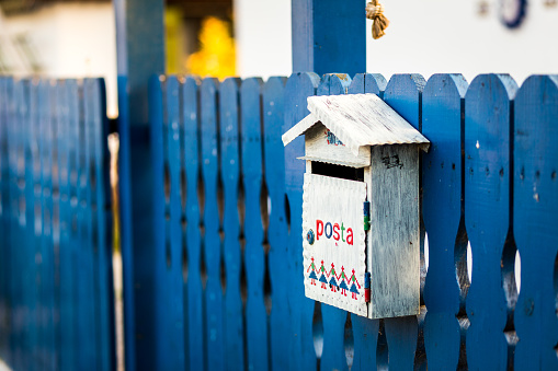 Close up color image depicting a white colored wooden mailbox attached to the blue picket fence on the outside of a front yard.