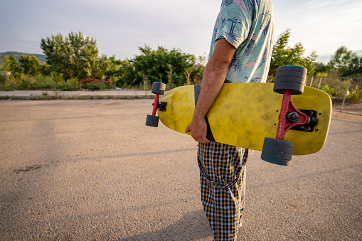 Caucasian man carrying skateboard on street.