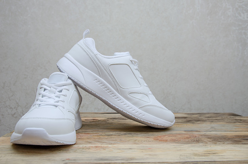 Beautiful pair of new white women's sneakers on a wooden background close up