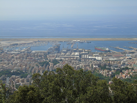 Genova, Italy – 07/30/2020: Beautiful scenic aerial view of the city, port, dam, sea, Cristoforo Colombo airport runway, containers shipping terminal, Pra, Voltri, and Sestri promontory from Monte Gazzo.