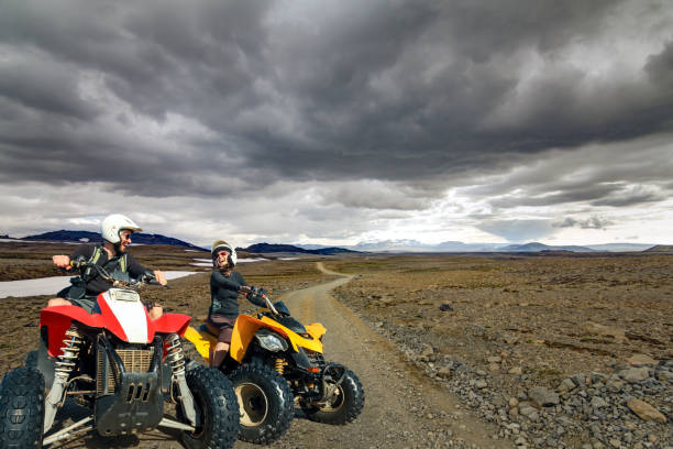 Happy smiling ATV quad driving man and woman traveling down a gravel road in Kaldidalur desert, Iceland. stock photo