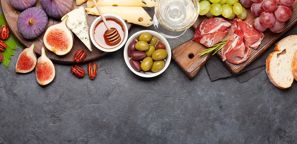 Antipasto plate with prosciutto, cheese, figs and grapes. Appetizer board and white wine. Top view flat lay with copy space