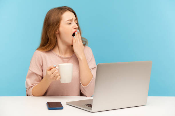 donna esausta sonnolenta seduta sul posto di lavoro con laptop e sbadiglio sensazione di sonnolento, tenendo tazza di caffè - yawning women drink coffee cup foto e immagini stock