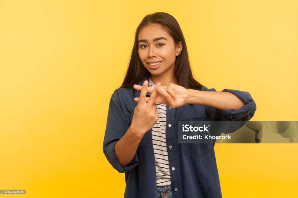 Hash sign, crossed fingers. Portrait of happy girl in denim shirt making hashtag gesture, web symbol of viral topic Hash sign, crossed fingers. Portrait of happy girl in denim shirt making hashtag gesture, web symbol of viral topic, famous comment and blogging. indoor studio shot isolated on yellow background Adulation Stock Photo