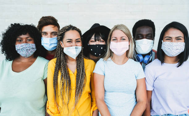 Young multiracial people wearing protective masks while smiling in camera - Happy friends during coronavirus outbreak - Social distance concept - Main focus on girl with yellow t-shirt face