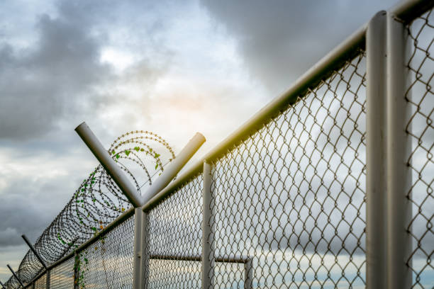 istock Prison security fence. Barbed wire security fence. Razor wire jail fence. Barrier border. Boundary security wall. Prison for arrest criminals or terrorists. Private area. Military zone concept. 1263565472