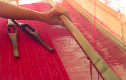 Woman working on weaving machine for weave handmade fabric. Textile weaving. Weaving using traditional hand weaving loom on cotton strands. Textile or cloth production in Thailand. Asian culture.