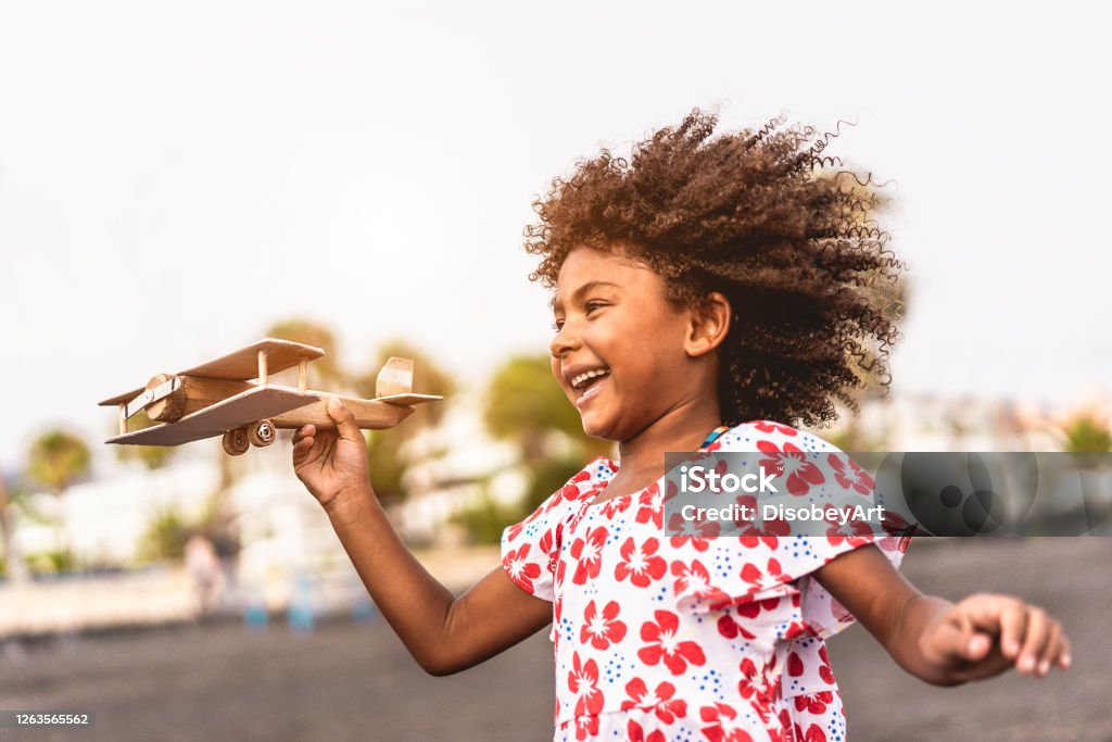 African kid running on the beach while playing with wood toy airplane at sunset, Travel and youth lifestyle concept - Main focus on hand holding plane Child Stock Photo