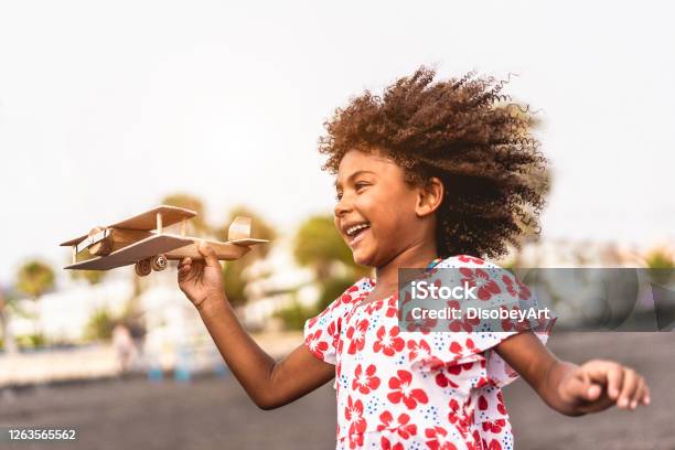 African Kid Running On The Beach While Playing With Wood Toy Airplane At Sunset Travel And Youth Lifestyle Concept Main Focus On Hand Holding Plane Stock Photo - Download Image Now