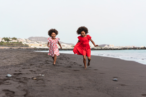 Afro twins sisters running on the beach together - Youth lifestyle and travel concept - Main focus on right kid face
