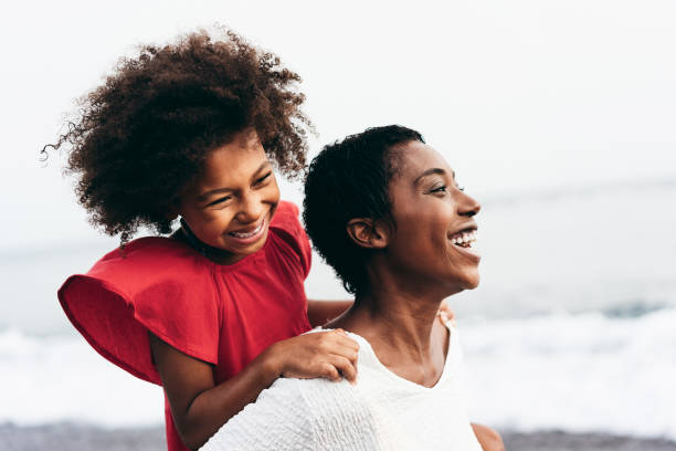 mère et fille noires courant sur la plage à l’heure du coucher du soleil pendant les vacances d’été - les gens de famille s’amusant ensemble en plein air - voyage et mode de vie de bonheur - se concentrer sur le visage de maman - face time photos et images de collection