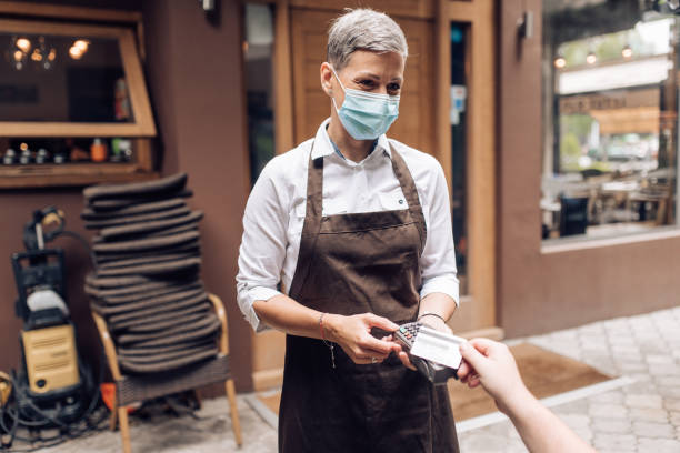 istock Waitress with a face mask at the cafe charging a bill to a customer 1263568049