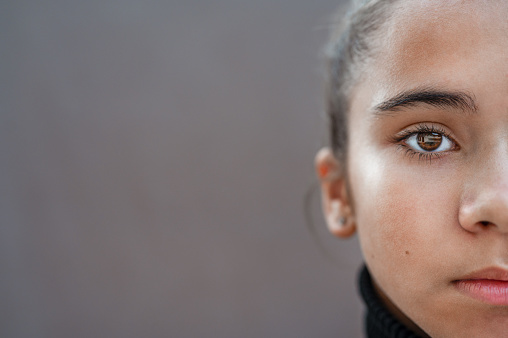 Portrait of a young caucasian girl. Half of her face on the right and grey copy space on the left side of image.