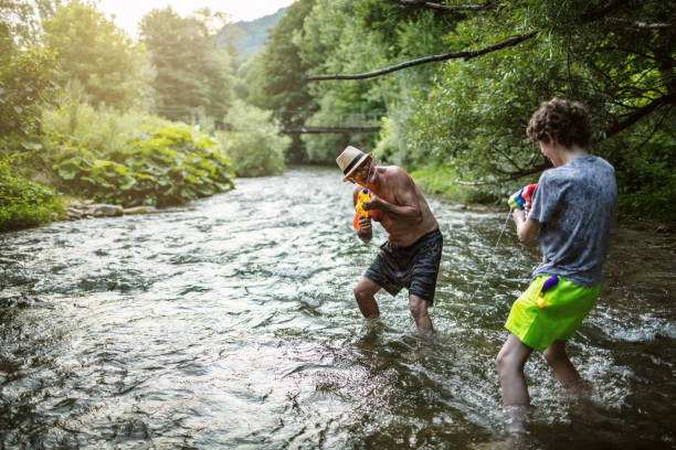 Grandfather having water fight with grandson on a river.