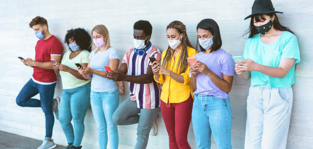 istock Young people wearing face safety masks using smart mobile phones while keeping social distance during coronavirus time - Technology and covid-19 spread prevention concept Focus on right girls hands 1263576000