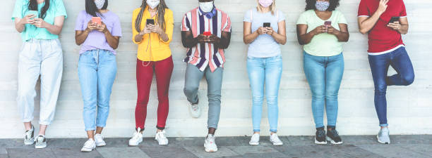 junge menschen tragen gesichtsschutzmasken mit mobiltelefonen, während sie während der coronavirus-zeit sozialen abstand halten - technologie und covid-19 spread präventionskonzept - schwerpunkt auf linken mädchenhänden - face time stock-fotos und bilder