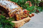 Traditional Christmas fruit cake on a wooden board in festive decoration, dark background.