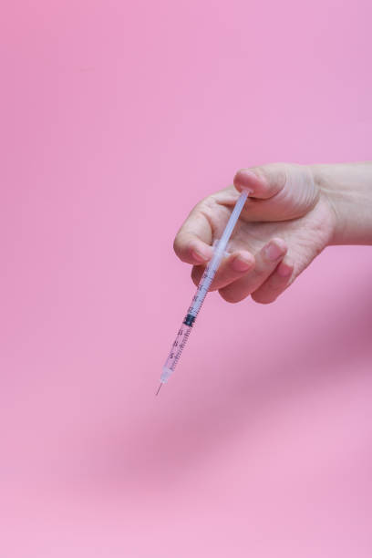 istock Hand holding syringe on pink background 1263602167