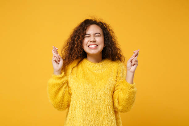 Pretty african american girl posing isolated on yellow orange background. People lifestyle concept. Mock up copy space. Waiting for special moment, keeping fingers crossed, eyes closed, making wish bonita chica americana africana posando aislada sobre fondo naranja amarillo. concepto de estilo de vida de la gente. simular el espacio de copia. esperando un momento especial, manteniendo los dedos cruzados, los ojos cerrados, haciendo deseo.