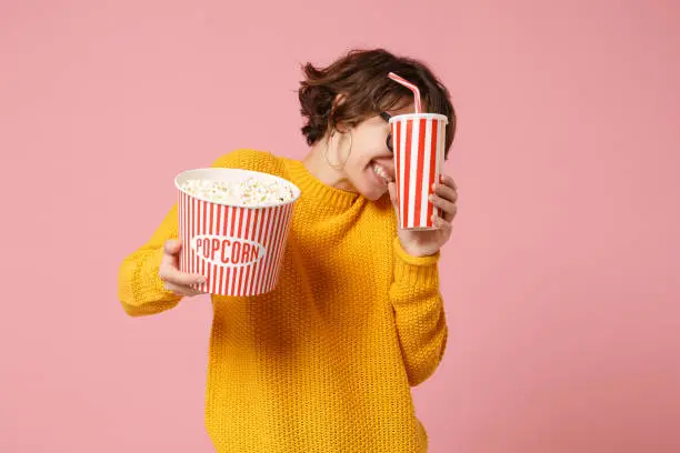 Scared young woman girl in 3d imax glasses posing isolated on pink background. People in cinema, lifestyle concept. Mock up copy space. Watching movie film, holding bucket of popcorn, cup of soda