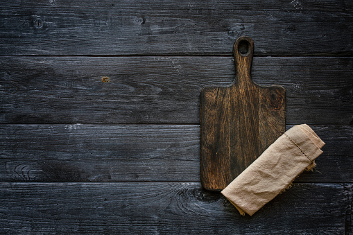 Wooden cutting board and linen napkin on black wooden table
