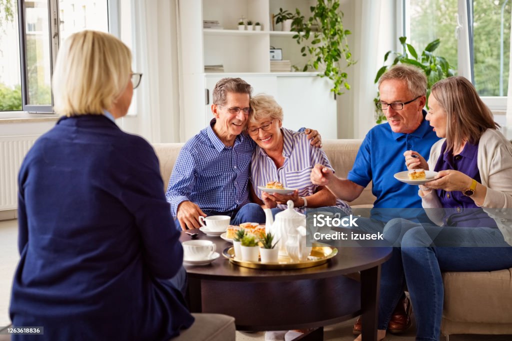 Cheerful senior people in retirement house Happy senior women and man spending time together in nursing home, talking with female social worker, drinking coffee, eating cakes. Mental Wellbeing Stock Photo