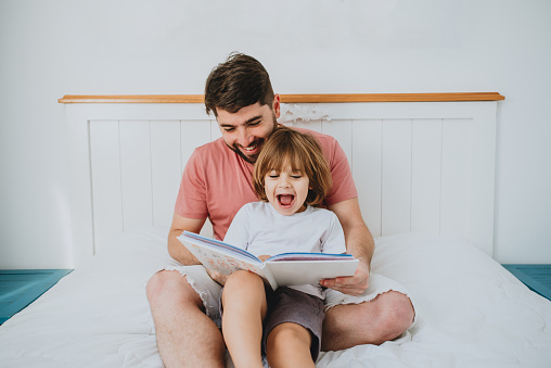 Father reading fun book to son in bed copy space