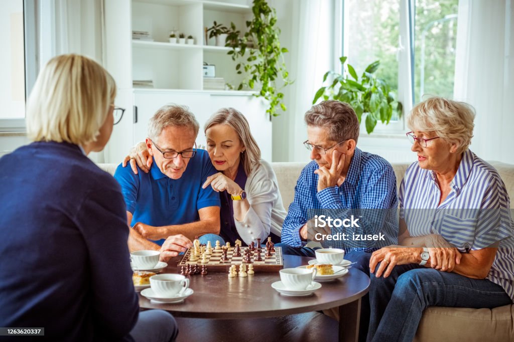 Senior people playing chess in retirement house Senior women and man spending time together in nursing home, playing chess in the living room. Chess Stock Photo