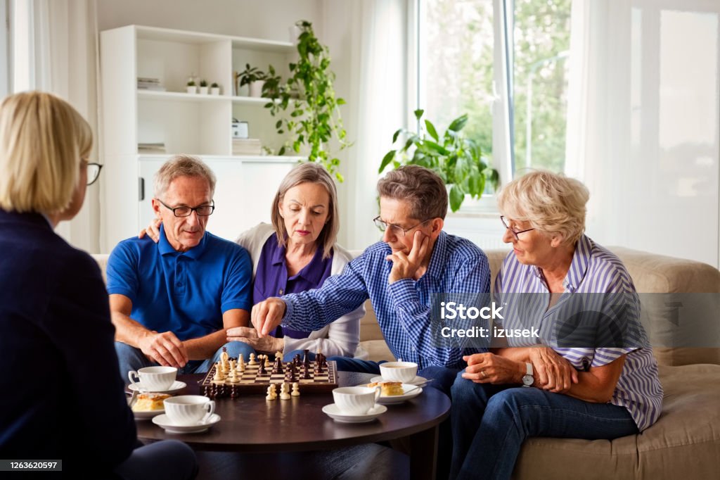 Senior people playing chess in retirement house Senior women and man spending time together in nursing home, playing chess in the living room. 70-79 Years Stock Photo
