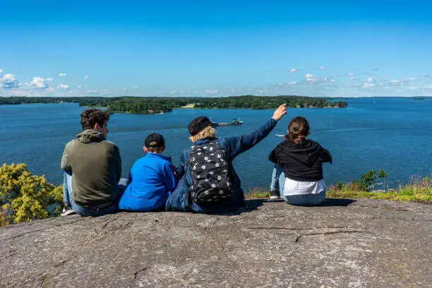Family sitting on a mountain top overlooking the water of Lake Mälaren against the horizon. Located at Gåseborg, an ancient settlement in Järfälla Sweden, horizontal composition.