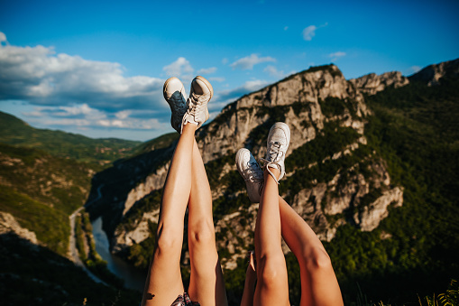 Two young female friends on top of a mountain lying on rock with legs crossed and raised