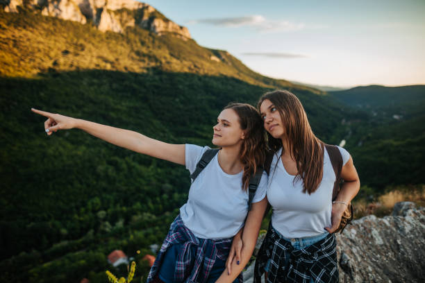 Two young female friends enjoying day and having fun on a top of a rocky mountain