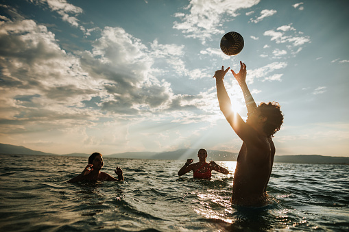 Friends having fun in the sea, playing volleyball in water during beautiful summer sunset