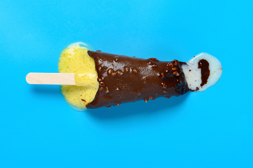 top view vanilla flavor with chocoate and peanuts outer popsicle starts melting on a blue background