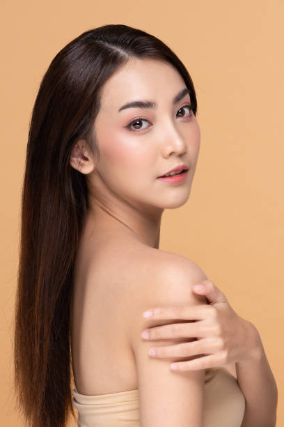 istock Beautiful Young Asian Woman Looking While Touching Shoulder feeling so happy and cheerful with healthy Clean and Fresh skin,isolated on Beige background,Beauty Cosmetology Concept 1263644321