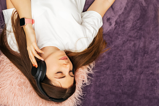 Woman wearing wireless headphones lying on the bed or floor listening to the music, top view