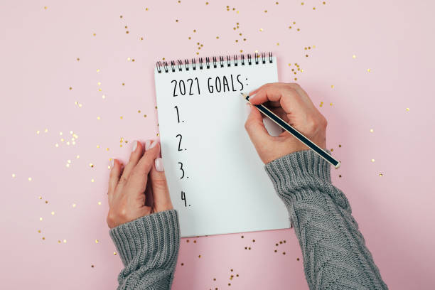 Happy New Year 2021. Woman's hand writing 2021 Goals in notebook Happy New Year 2021. Woman's hand writing 2020 Goals in notebook decorated with Christmas decorations on the tricolor background. Top view, flat lay 2021 photos stock pictures, royalty-free photos & images